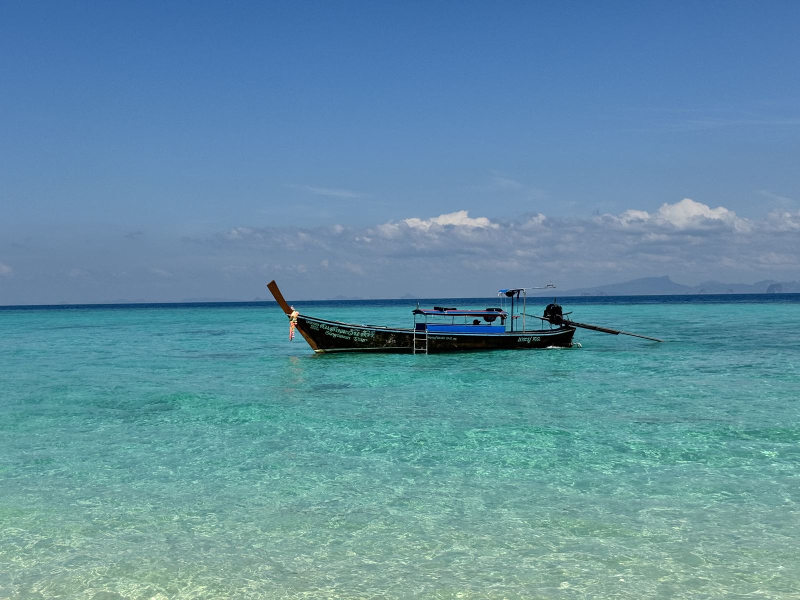 A wooden longtail boat on calm, clear shallow water