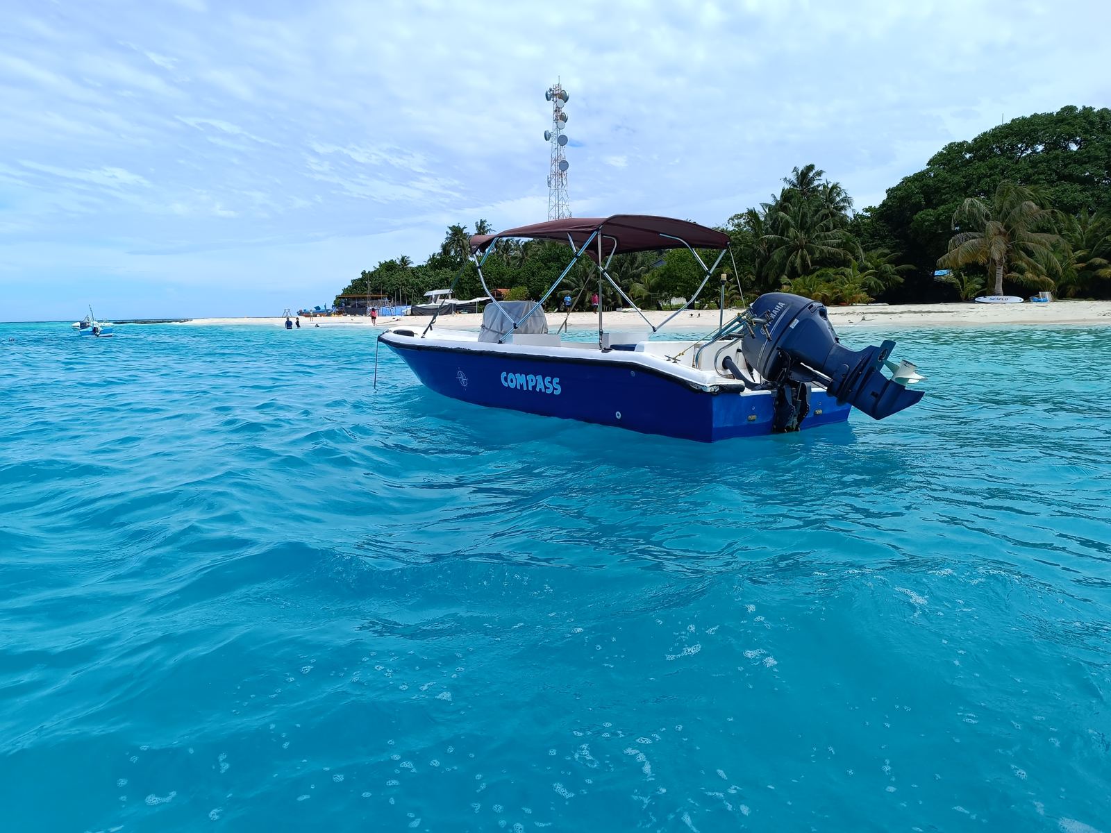 A dive boat anchored in clear turquoise water near a sandy beach